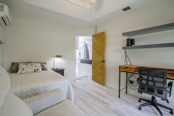 A bedroom with a bed, bedside table, lamp, and a desk with a chair.