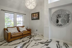 A room with a brown leather sofa, a large abstract tree wall art, and a painting above it. - Near Shopping & Dining! Family Escape in Mcallen (McAllen)
