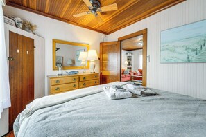 Een slaapkamer met een houten plafond, een bed met een witte deken, een kapstok met spiegel en een schilderij aan de muur.
