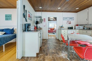 Een compacte keuken met witte kastjes, een koffieapparaat en een eethoek met rode stoelen.