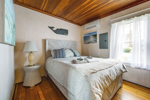 Un dormitorio con una cama, una lámpara de noche, un aire acondicionado instalado en la pared y una ventana con cortinas.