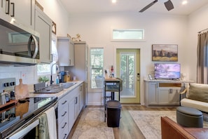 A modern kitchen with a built-in microwave, a dining area with a table and chairs, and a living room with a sofa and a TV. - Screened Porch w/ Fireplace! copperhill Tiny Home (Copperhill)