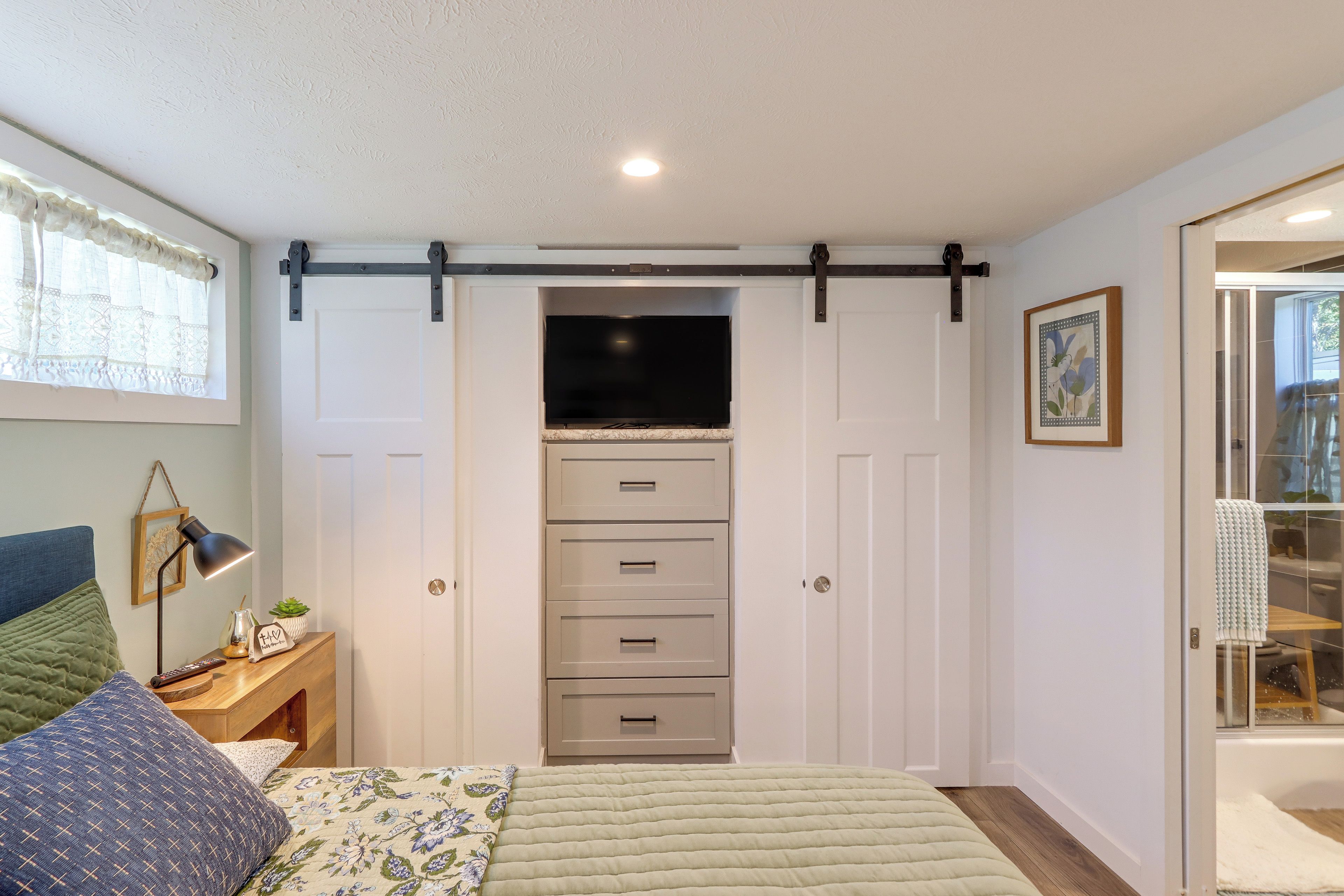 A bedroom with a bed, a nightstand, a desk, a sliding closet door, and a window with curtains.