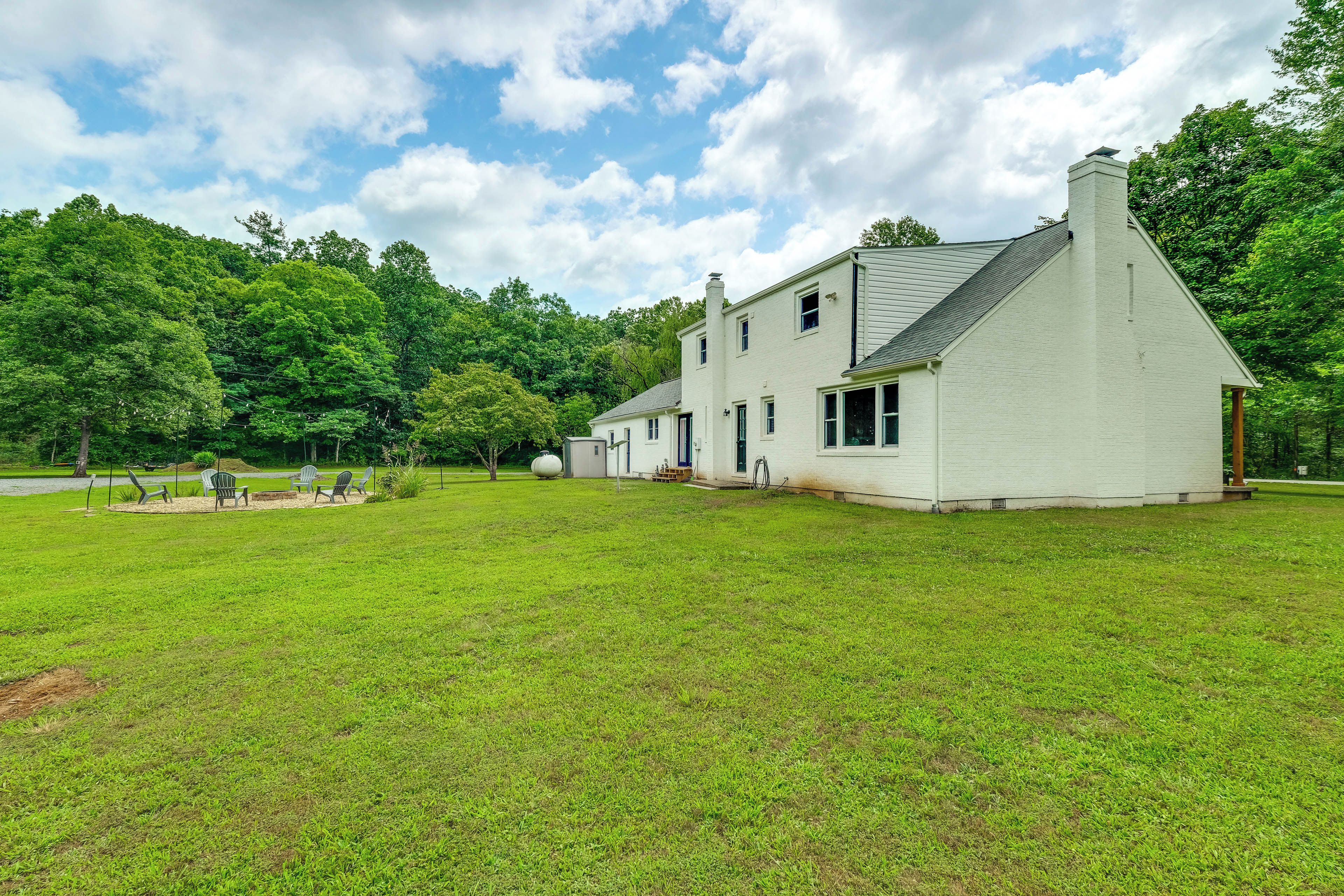 A white two-story house with a sloped roof, surrounded by a well-maintained lawn and trees.