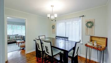 Une salle à manger avec une table en bois, six chaises, un lustre et une fenêtre ornée de rideaux légers.