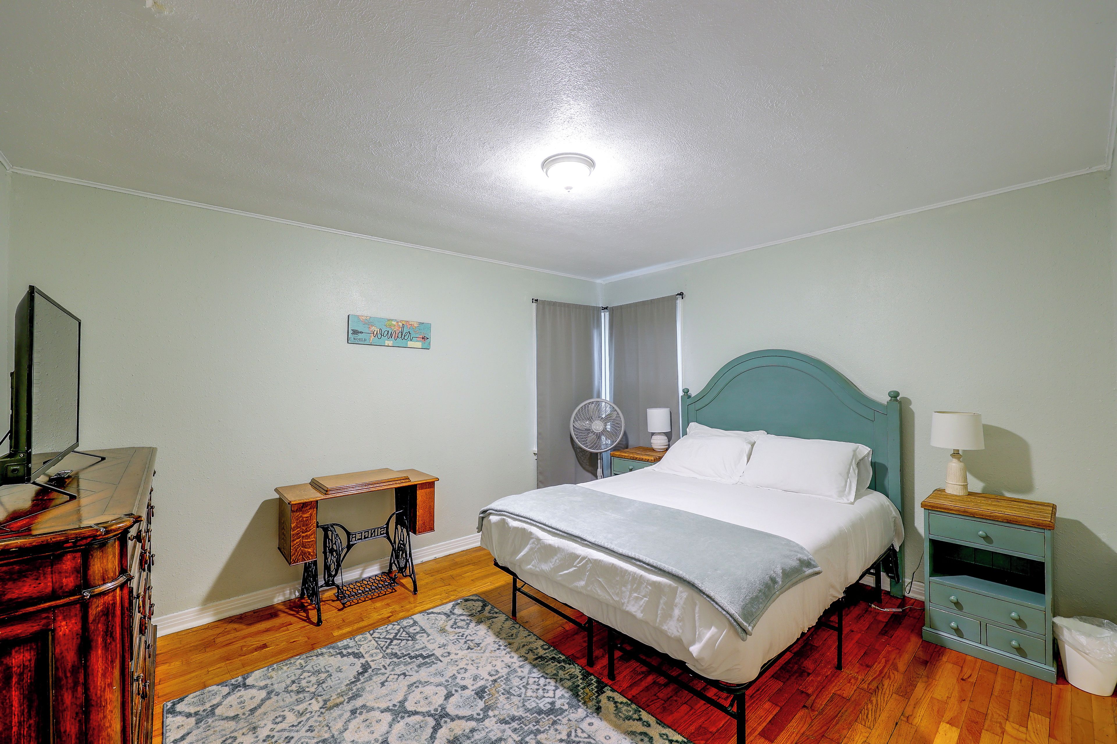Une chambre à coucher comprenant un lit, une commode, une machine à coudre, un ventilateur et une table de chevet.