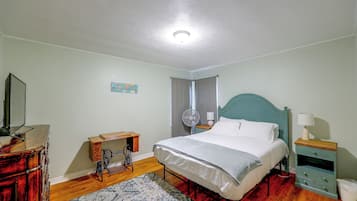 Un dormitorio con cama, cómoda, máquina de coser, ventilador y mesita de noche.
