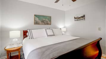 Quarto com cama, abajures, ventoinha no teto e duas pinturas penduradas na parede.
