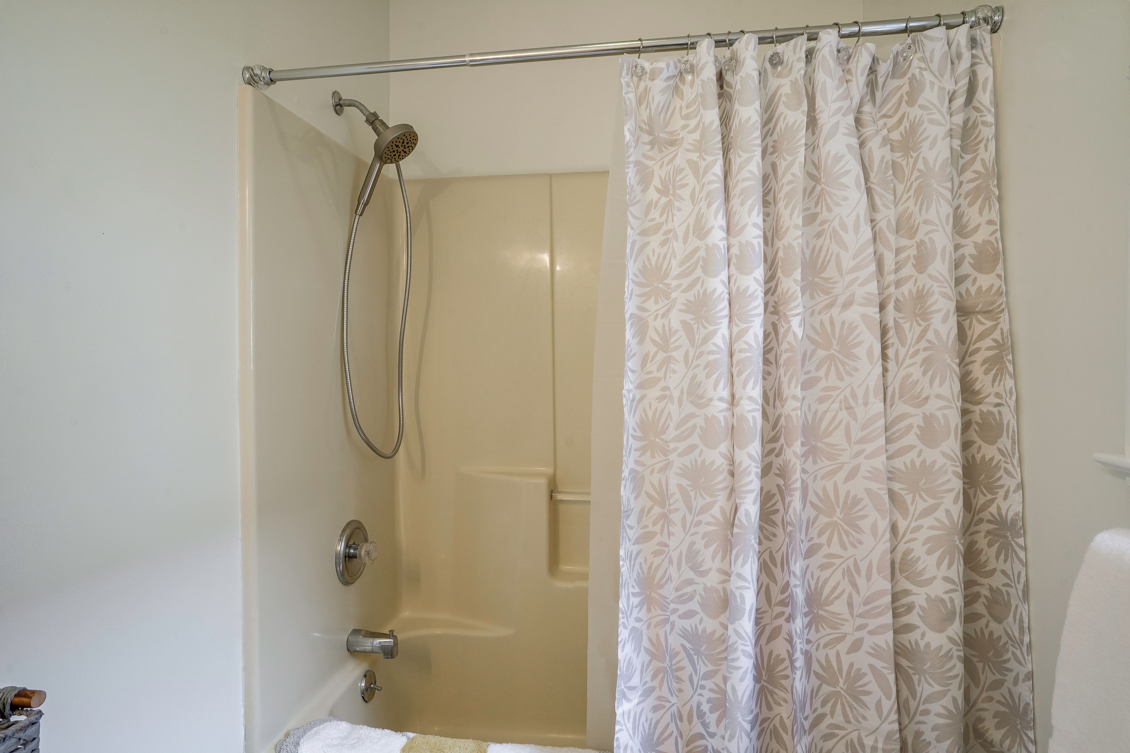 A bathroom with a shower curtain, a handheld showerhead, and a towel rack.
