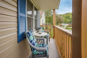 A covered porch with a table and two chairs, a wooden railing, and a view of a residential street.