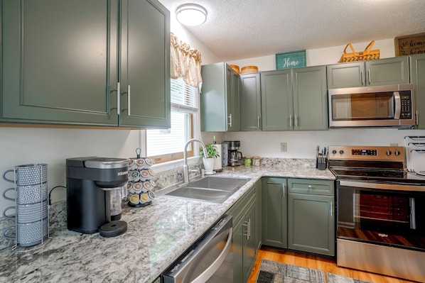 A kitchen with green cabinets, a built-in microwave, a coffee maker, and a stove.