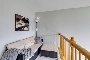 A modern living room with a sofa, a throw blanket, a floor lamp, and a wooden staircase railing. - Shakopee Townhome Near Valleyfair & Mystic Lake (Shakopee)