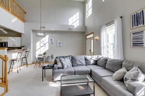 A modern living room with a grey sectional sofa, a glass coffee table, and a dining area with chairs and a small table. - Shakopee Townhome Near Valleyfair & Mystic Lake (Shakopee)