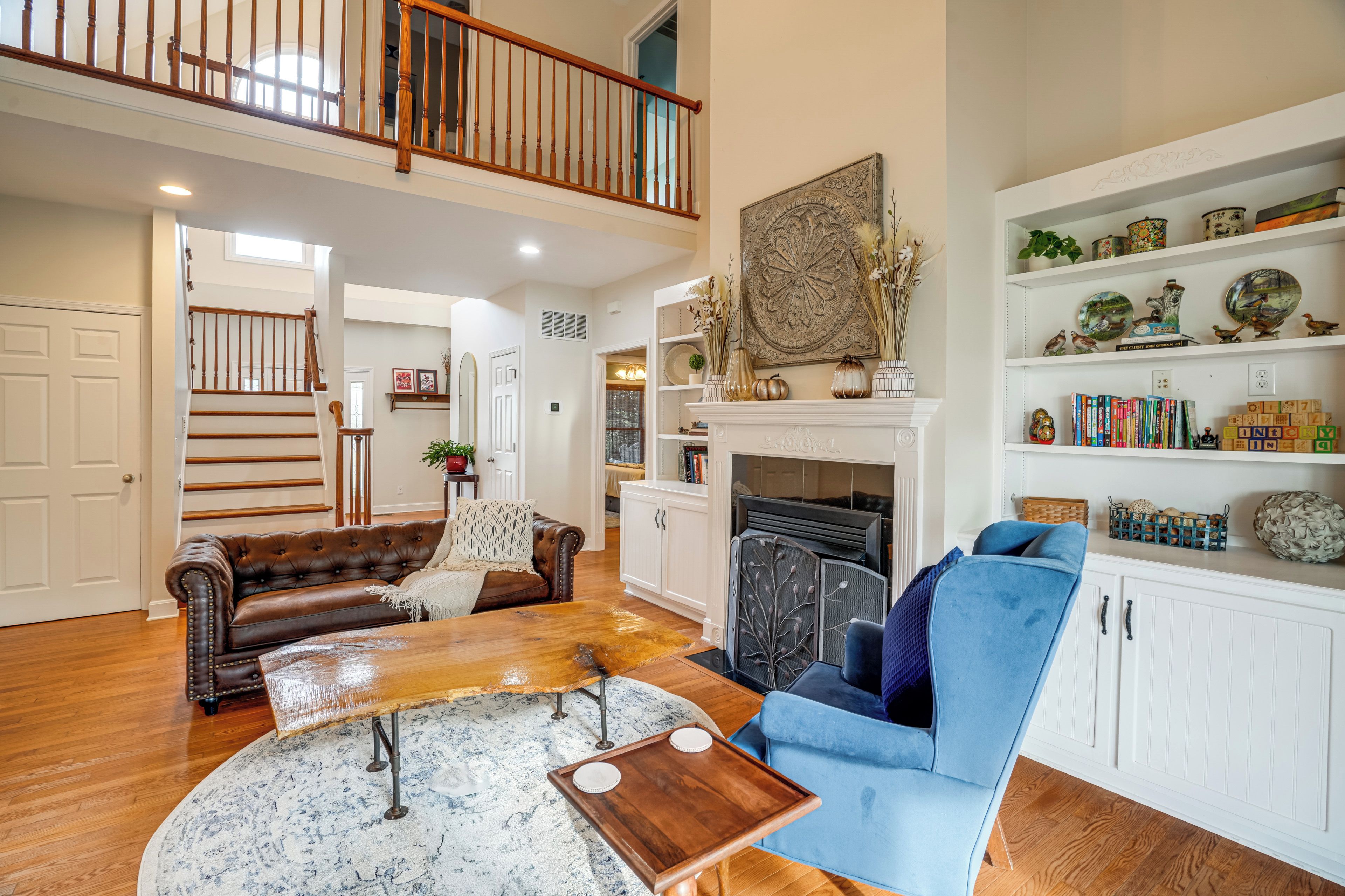 A spacious living room with a fireplace, a blue armchair, a brown leather sofa, and a wooden coffee table.