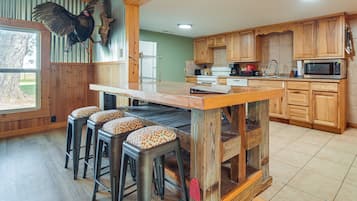 Une cuisine avec des meubles de rangement en bois, un îlot central avec des tabourets, un four à micro-ondes et un oiseau suspendu.