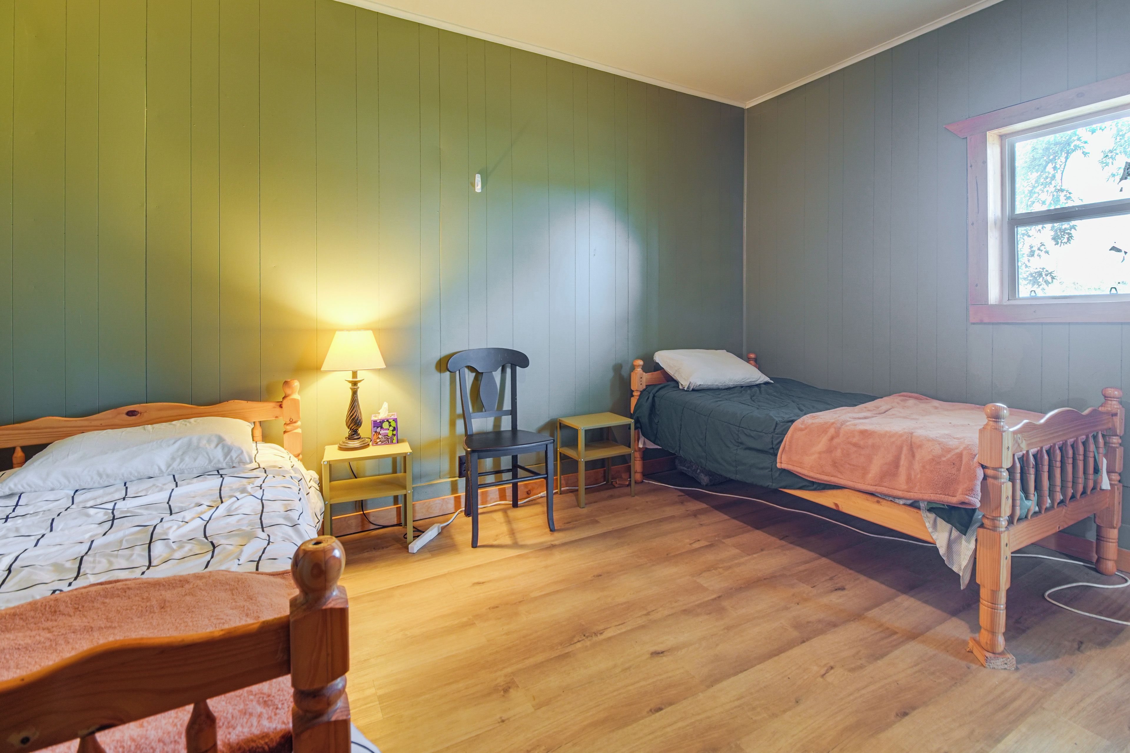 A room with two wooden beds, a chair, a small table, and a window.