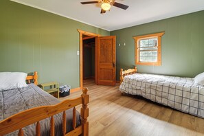 A room with two wooden beds, a ceiling fan, a window with a view, and a door leading to another room.