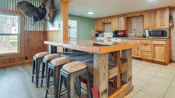 A kitchen with wooden cabinets, a central island with stools, a microwave, and a hanging bird.
