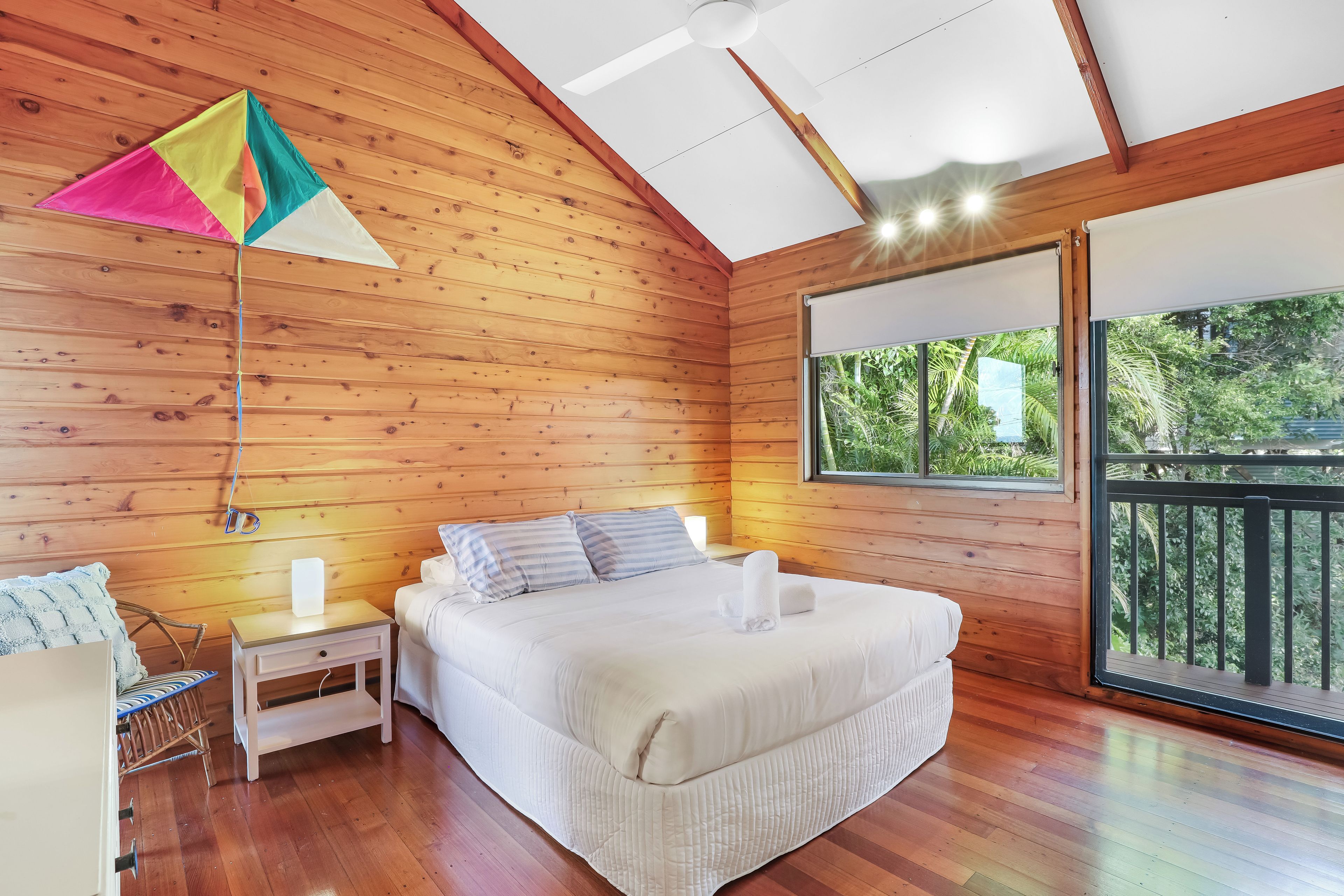 Habitación de cabaña de madera con cama, mesita de noche y ventana con vistas a follaje.