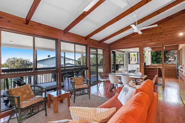 A spacious living area with a wooden ceiling, large windows, and a view of the outdoors.