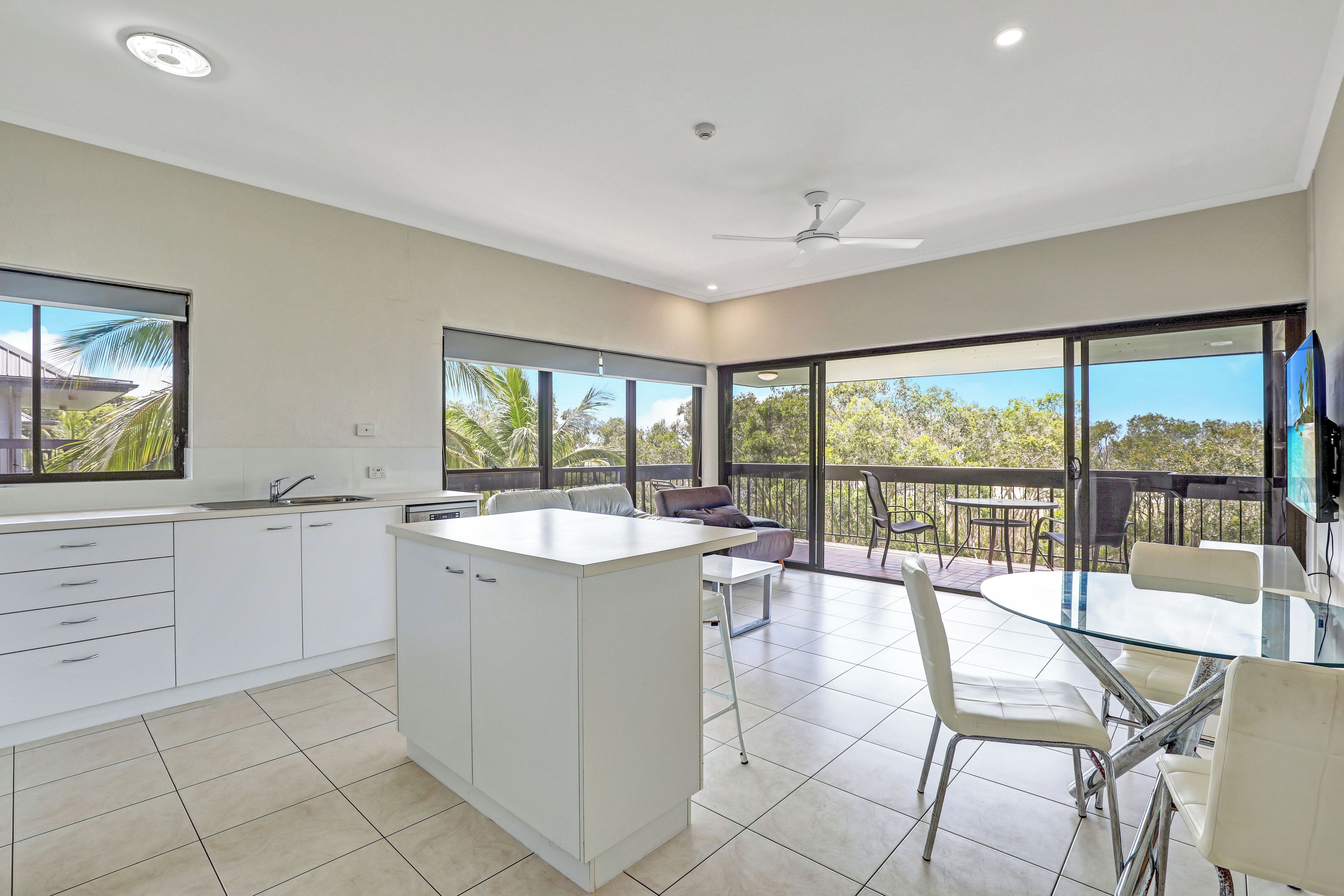 A modern kitchen with a central island, a dining area with a glass table, and a balcony with outdoor seating.