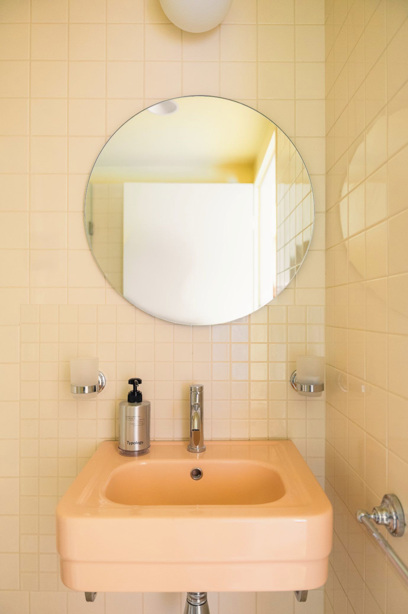 Un baño con un espejo redondo, un lavabo y dos dispensadores de jabón.