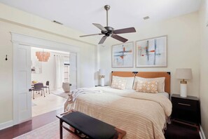 A bedroom with a bed, a ceiling fan, artwork on the wall, and a nightstand with a lamp. - The Lincoln Retreat | 3 Blocks to Forsyth | Shops (Savannah)