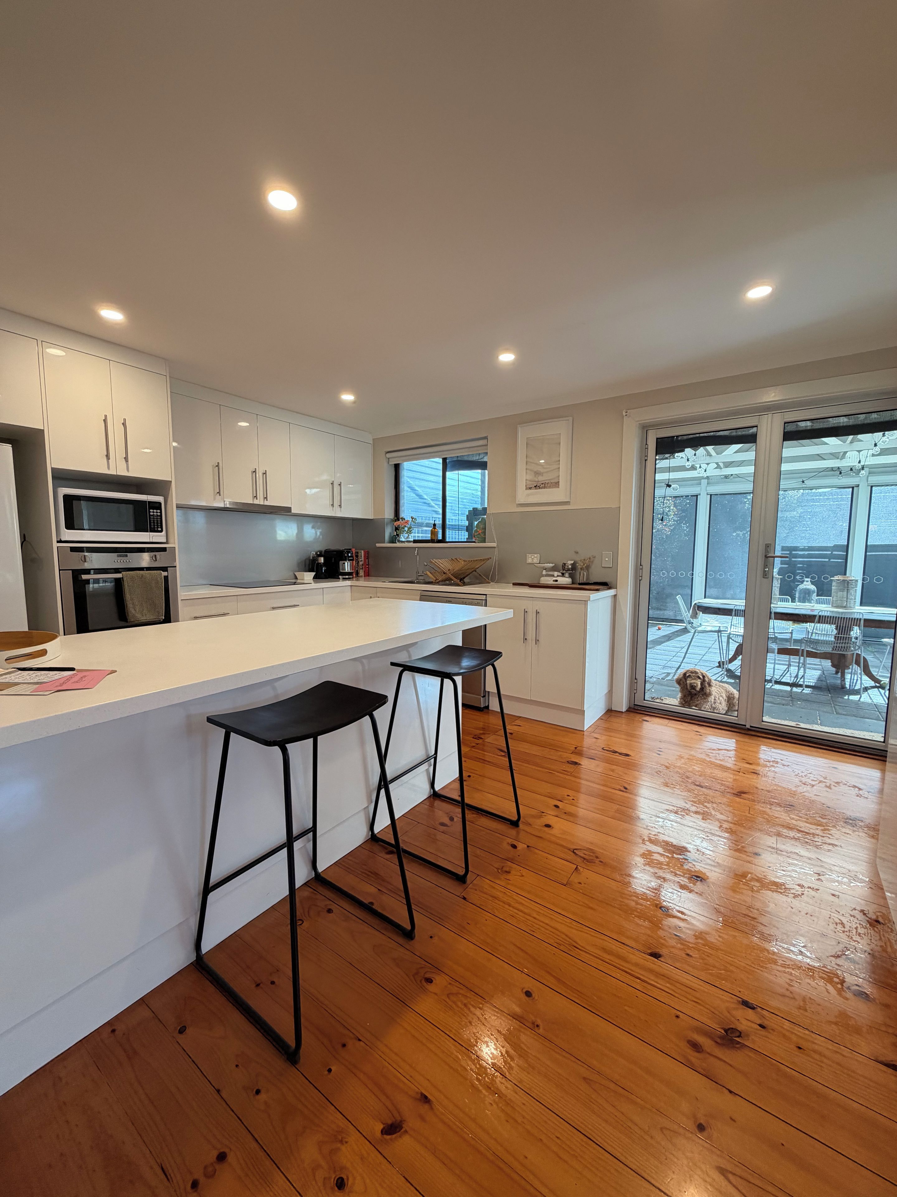 A modern kitchen with white cabinets, a microwave, and a large island with two stools.