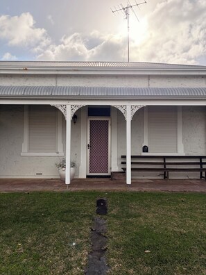 A building with a corrugated metal roof, a white facade, and a covered entrance with decorative arches. - Rêverie | cosy coastal cottage, walking distance to cafes and beach (Kingston SE)