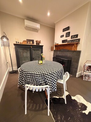 A cozy room with a fireplace, a checkered table, and a cowhide rug. - Rêverie | cosy coastal cottage, walking distance to cafes and beach (Kingston SE)