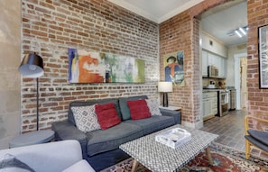 A living room with a sofa, a coffee table, and a lamp. There is a kitchen visible in the background. - Sleep 12 | 2 Garages | Pets | Steps to Broughton (Savannah)
