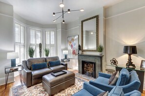 A living room with a fireplace, a large mirror, and a modern chandelier. - Sleep 12 | 2 Garages | Pets | Steps to Broughton (Savannah)