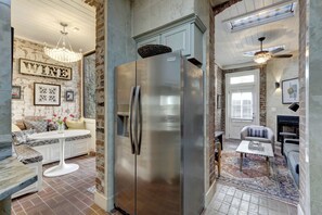 A modern kitchen with a stainless steel refrigerator, a dining area with a white table and bench, and a cozy seating area with patterned cushions. - Sleep 12 | 2 Garages | Pets | Steps to Broughton (Savannah)
