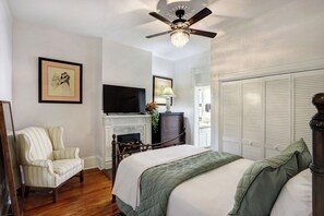 A bedroom with a bed, a chair, a television, a fireplace, and a wardrobe. - Sleep 12 | 2 Garages | Pets | Steps to Broughton (Savannah)