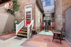 A brick building with a red door, a white staircase, and a small outdoor seating area with a table and chairs. - Sleep 12 | 2 Garages | Pets | Steps to Broughton (Savannah)