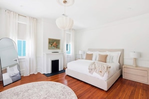 A bedroom with a bed, bedside tables, a fireplace, and a mirror. - The Upper Olmstead - 1800s Victorian Near Forsyth (Savannah)