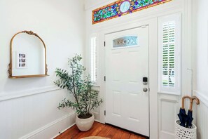A hallway with a white door, a potted plant, a mirror, and a wall-mounted clock. - The Upper Olmstead - 1800s Victorian Near Forsyth (Savannah)