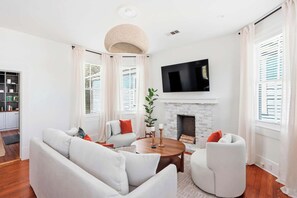 Ein modernes Wohnzimmer mit Kamin, weißen Sofas, einem Couchtisch und einem Fernseher über dem Kamin.