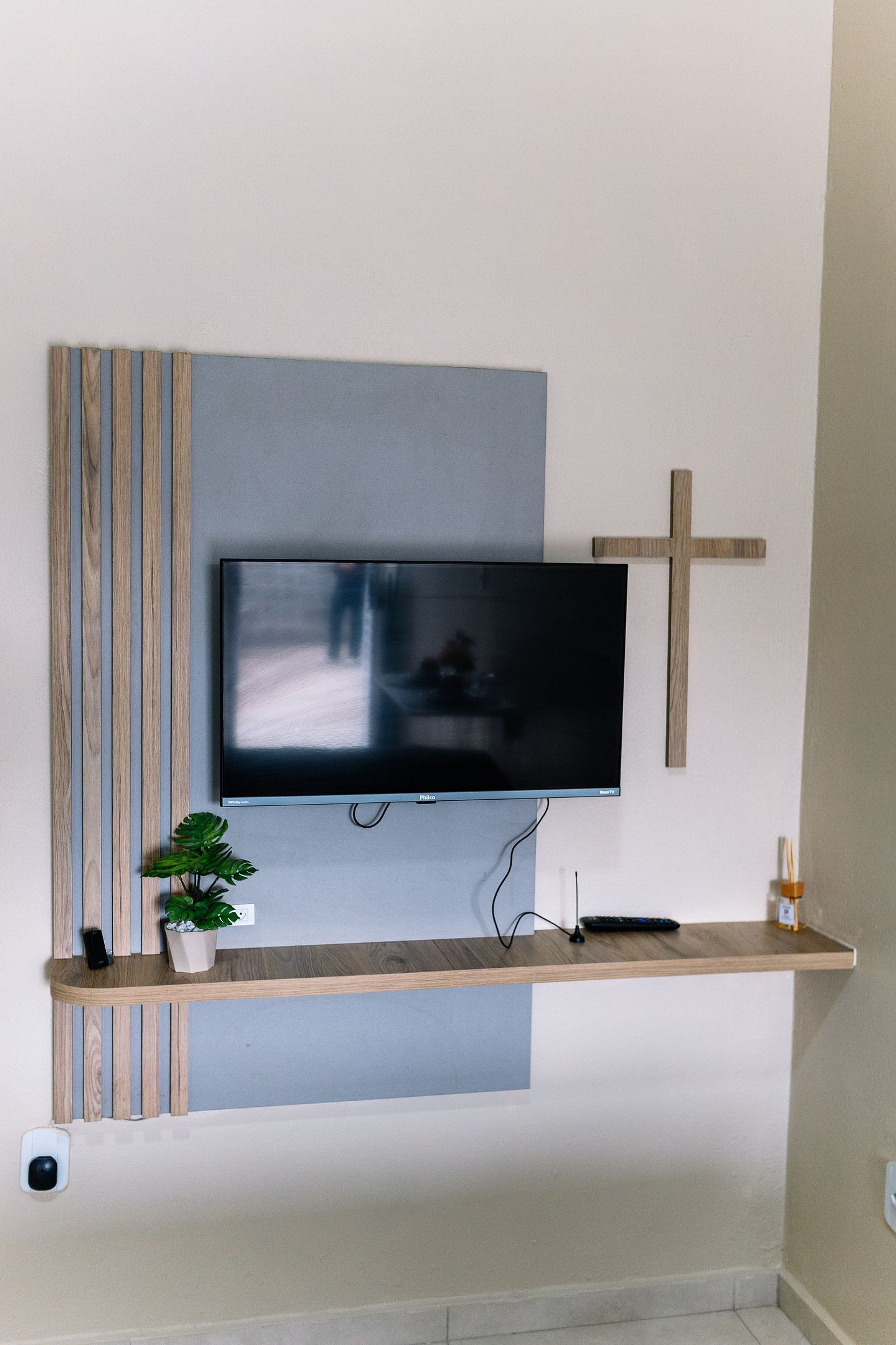 Un téléviseur à écran plat fixé au mur, avec une étagère en bois en dessous.