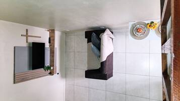 Quarto com cama, uma cruz na parede, uma planta pequena e uma mesa com um prato decorativo.
