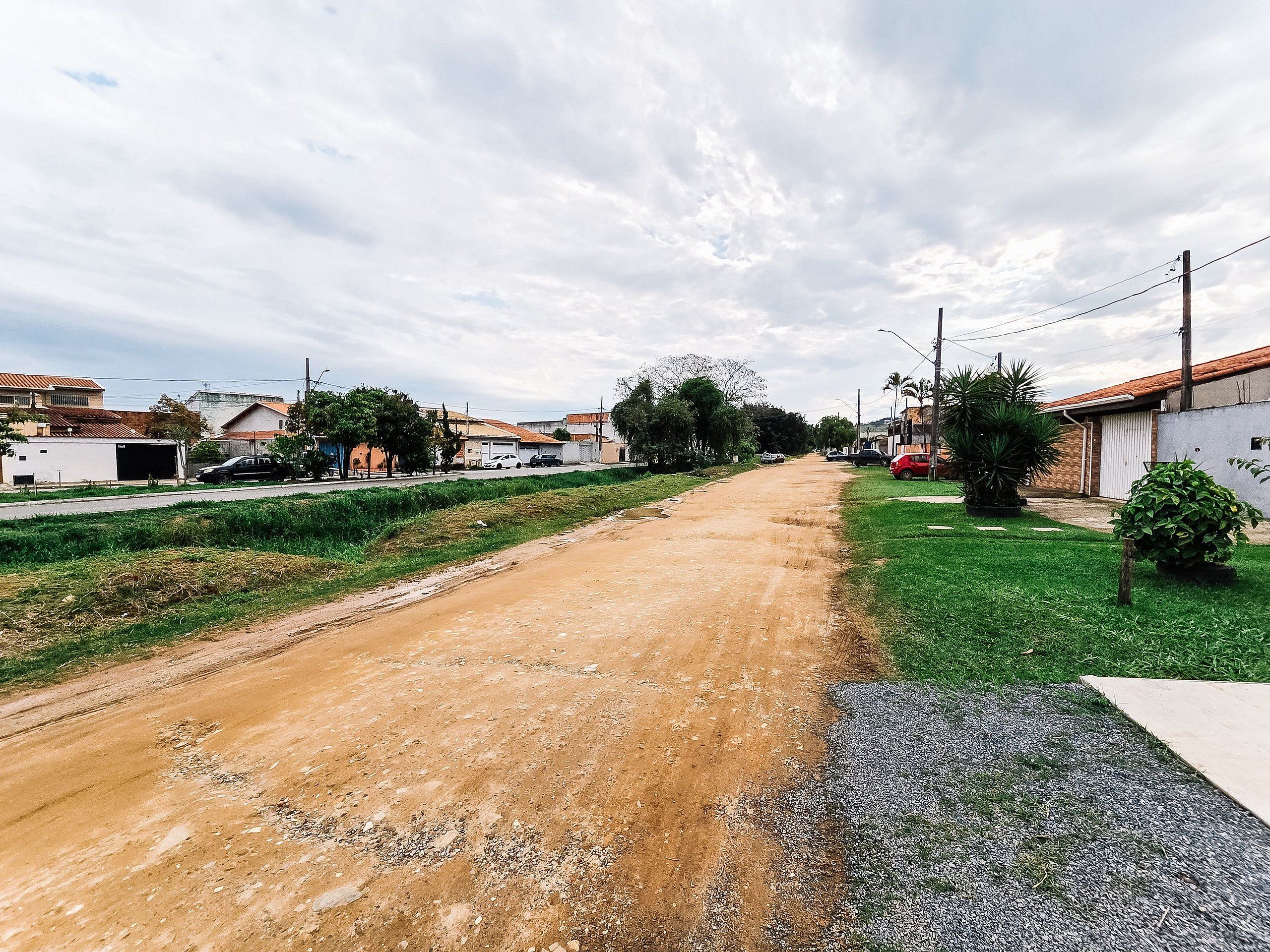 Une route de campagne bordée de maisons des deux côtés, un chemin de terre et une zone herbeuse.