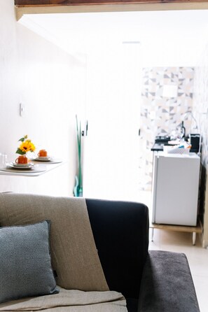 Una sala de estar con un sofá, una mesa de centro con un florero y una cocina al fondo.