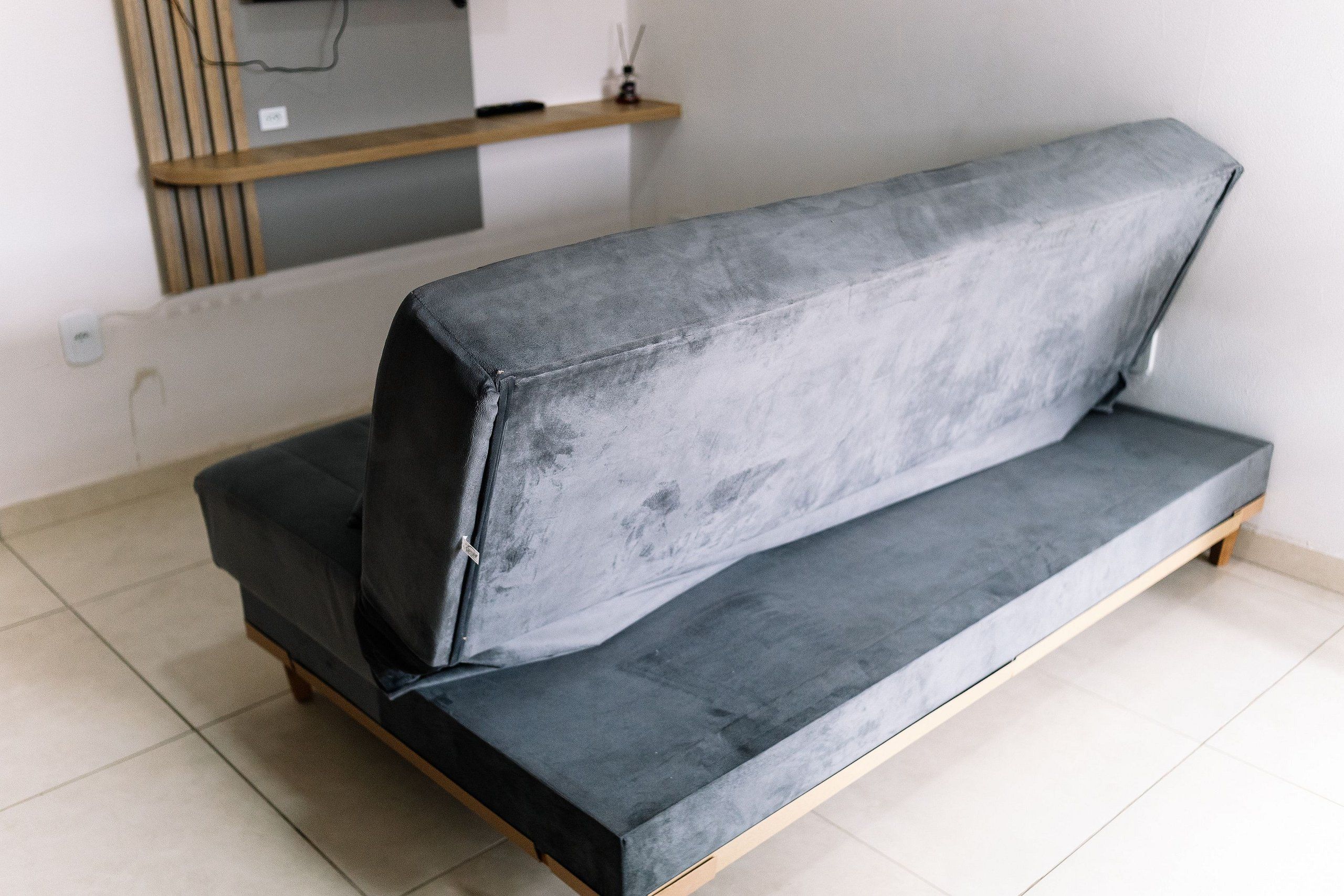 Un sofá gris con patas de madera en una habitación con paredes blancas y suelo de baldosas.
