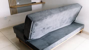 Un sofá gris con patas de madera en una habitación con paredes blancas y suelo de baldosas.