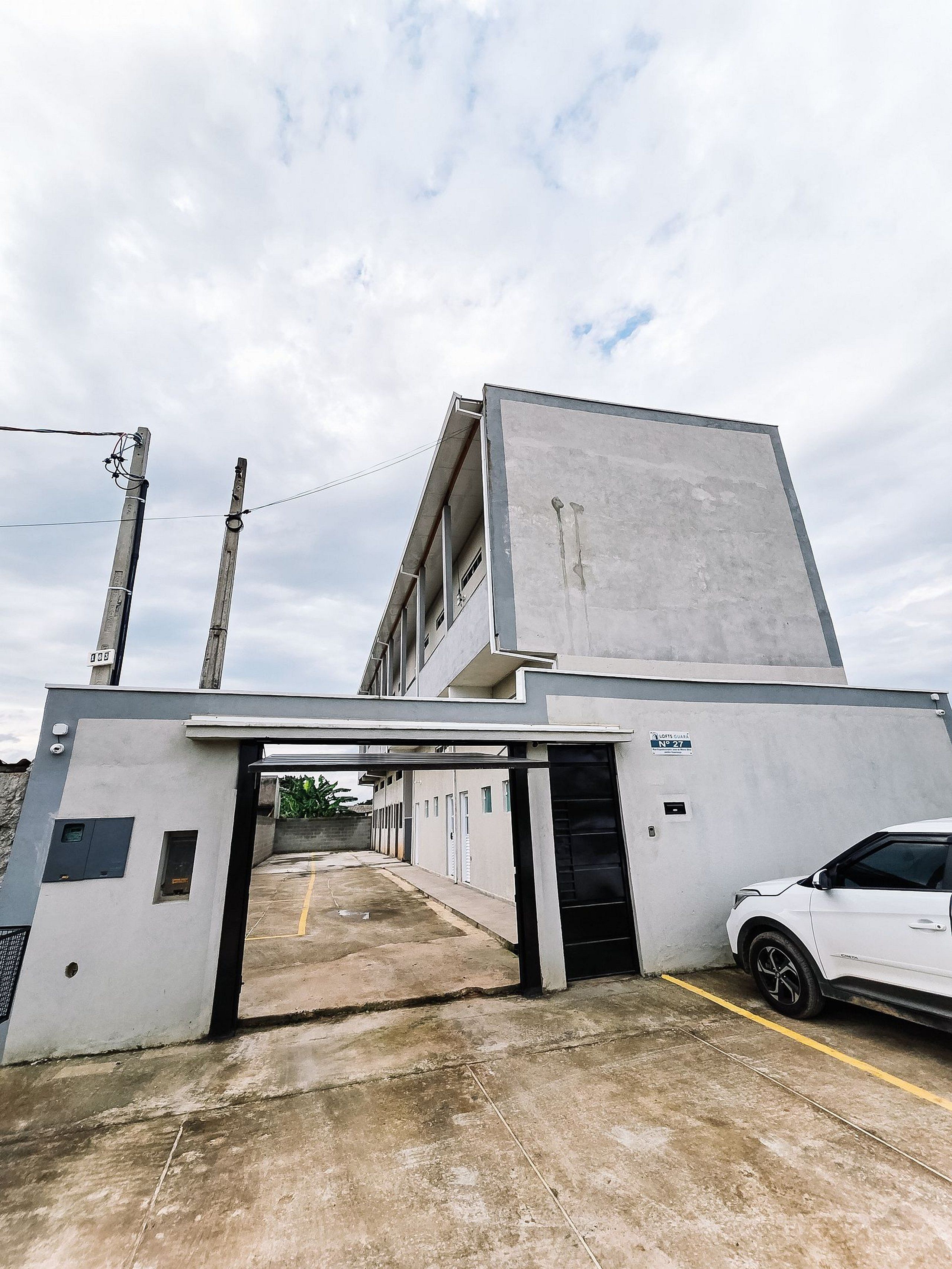 Edifício com entrada coberta, um carro estacionado no interior e céu claro.