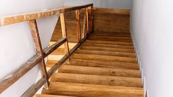 A wooden staircase with a metal handrail, leading to a landing with a white wall and a light switch.
