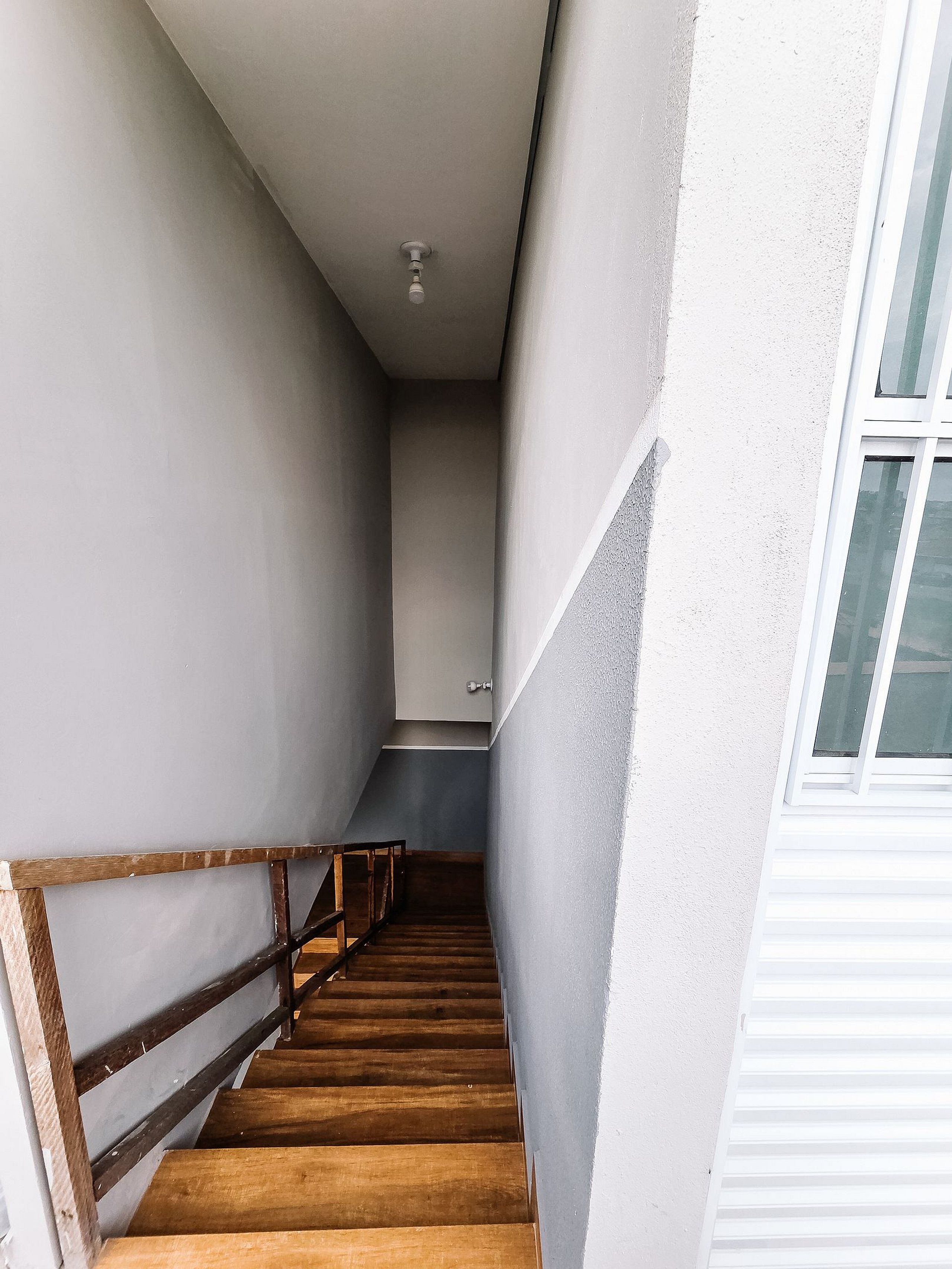 Una escalera estrecha de madera con barandilla metálica, que conduce a un rellano con una puerta.