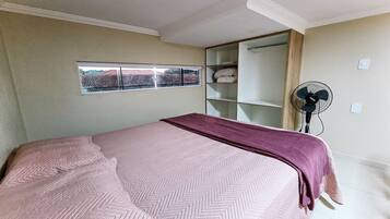 A bedroom with a bed, a window, a wardrobe, and a standing fan.