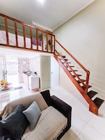Una sala de estar con un sofá, una mesa de comedor con sillas, una zona de cocina y una escalera de madera.