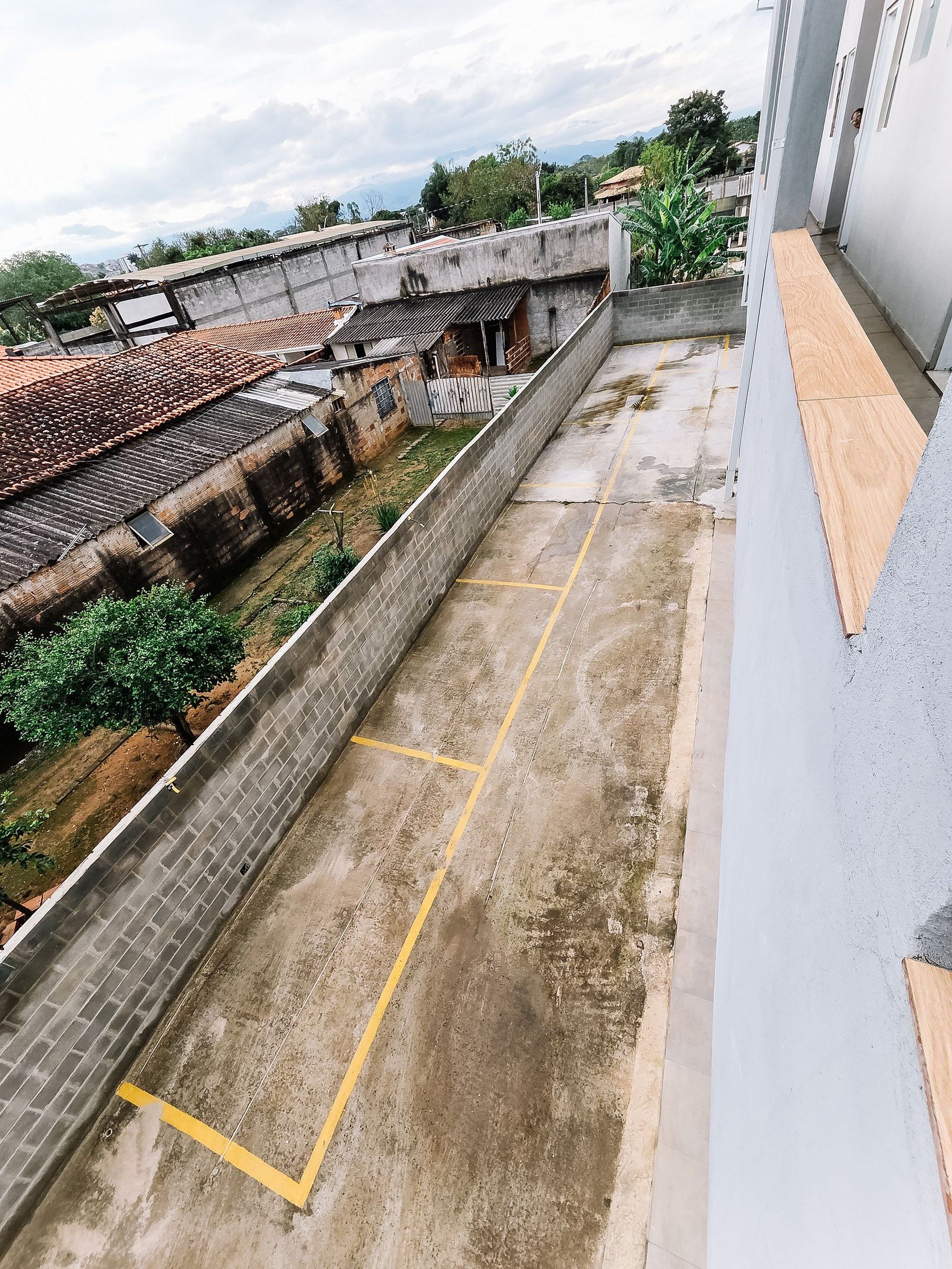 A rooftop with a concrete barrier, a paved area with yellow lines, and a view of buildings with red-tiled roofs.
